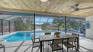 A covered outdoor pool area with a table and chairs, a ceiling fan, and a view of a lake and greenery. - Poolside Oasis - Modern spacious 3 bedroom, 2 bathroom private pool home in Sarasota near Siesta Key (Sarasota)