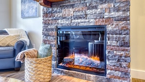 A stone fireplace with a glass front, a woven basket with decorative items, and a blue sofa with a blanket.