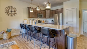 A modern kitchen with a central island, bar stools, stainless steel appliances, and pendant lighting.
