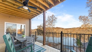 A wooden deck with a table and chairs, overlooking a body of water and trees.