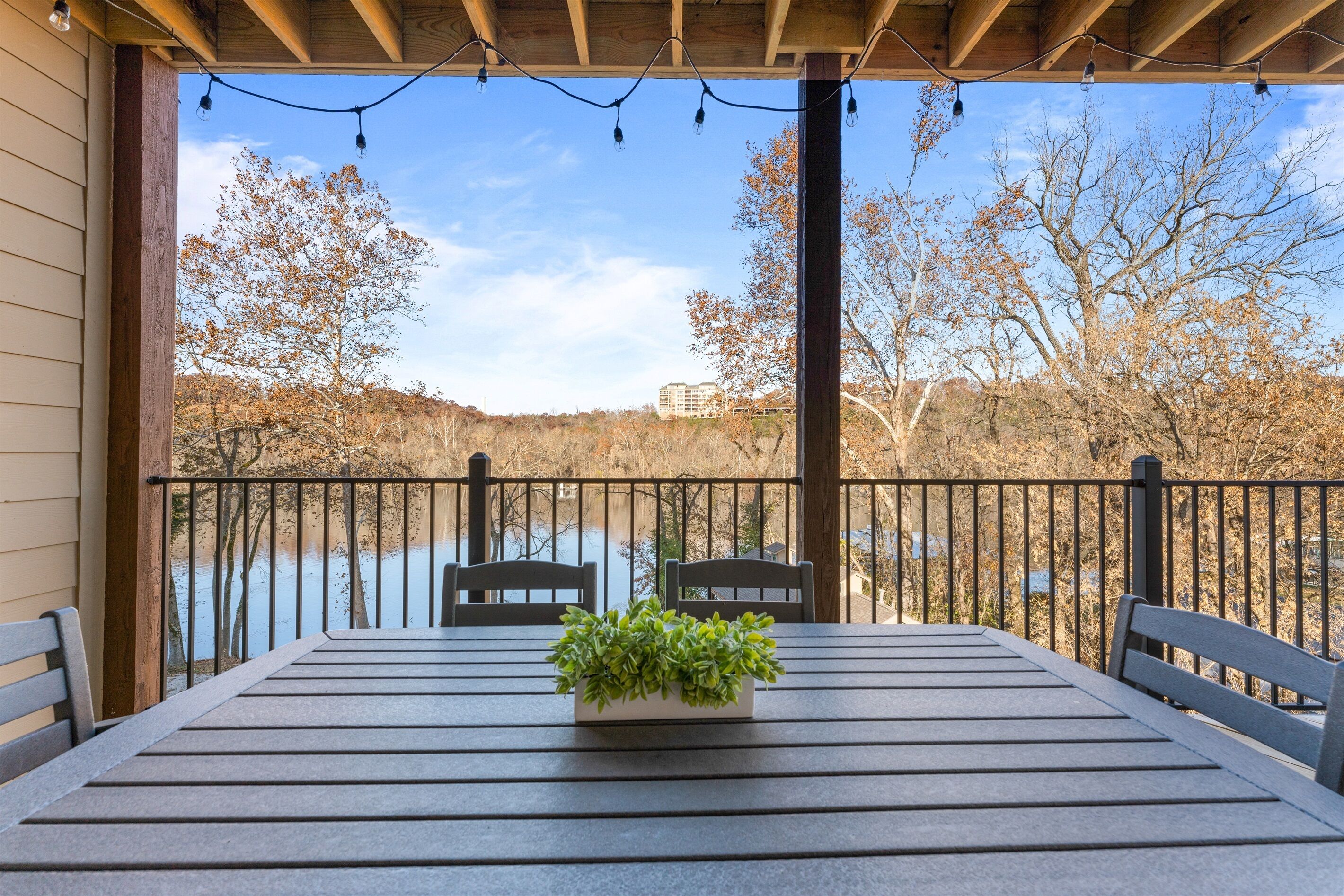 A covered patio with a table and chairs, overlooking a river and trees.