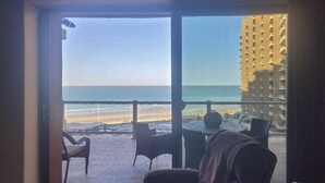 A room with a view of the beach and ocean. There are two chairs and a table in the foreground.