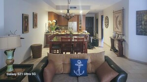 A modern living room with a Galaxy S21 Ultra 5G on a table, a sofa with a cushion, a dining area with chairs, and a kitchen in the background.