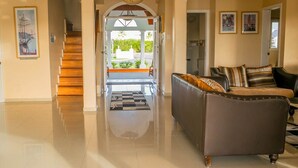A spacious living area with a polished floor, a sofa, and a staircase leading to an outdoor area. - Affordable Ariyana sleeps 10 in Tobago Plantations (Lowlands)