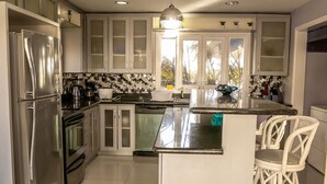 A modern kitchen with stainless steel appliances, white cabinetry, and a central island with bar stools. - Affordable Ariyana sleeps 10 in Tobago Plantations (Lowlands)