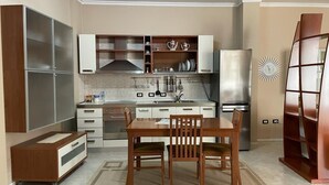 A modern kitchen with a central island, white cabinets, stainless steel appliances, and a decorative wall clock. - Entire Apartment in the Center of Tirana (Tirana)