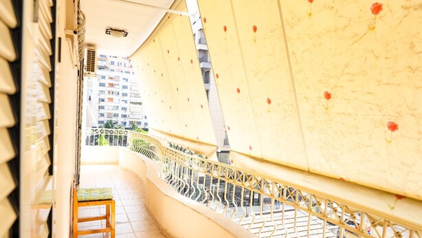 A balcony with a metal railing, a small wooden stool, and a view of buildings in the background. - Entire Apartment in the Center of Tirana (Tirana)