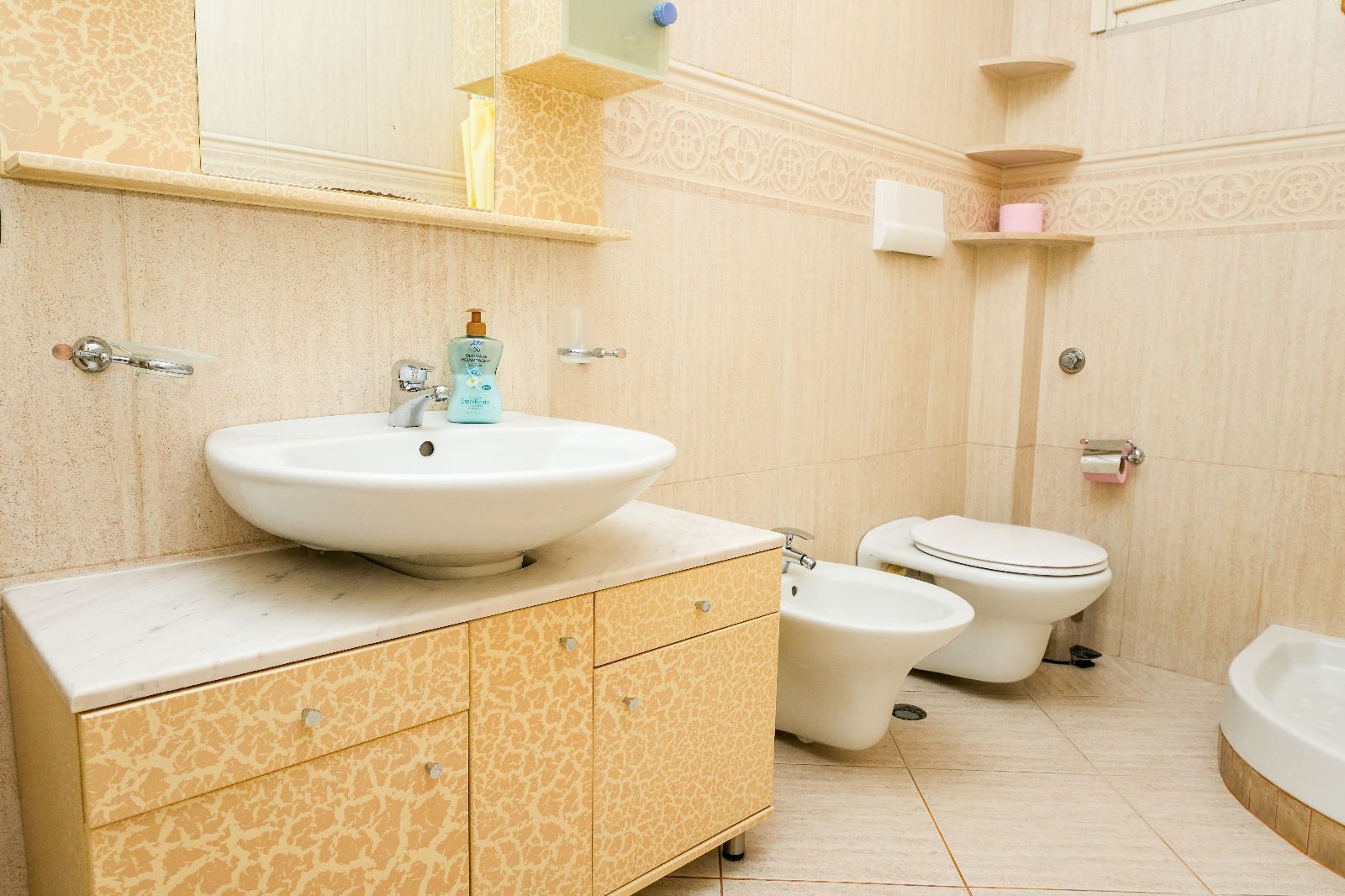 Een badkamer met een groot wastafel, twee toiletten, een douchetoilet en een bad.