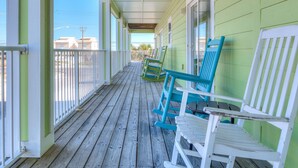 A covered porch with wooden railings and a series of rocking chairs. - Sea Urchins, North & South Units. 10 BR 10BA. Beachview. The Beach, so close, for less! Pool. (Gulf Shores)