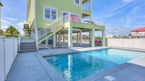 A two-story building with a pool, stairs leading to a balcony, and a fenced area with red chairs. - Sea Urchins, North & South Units. 10 BR 10BA. Beachview. The Beach, so close, for less! Pool. (Gulf Shores)