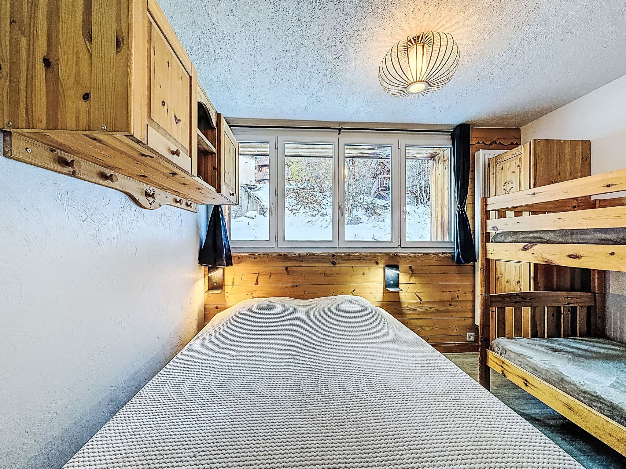 Un cuarto acogedor con una cama litera, una ventana con vista a un paisaje nevado y una lámpara colgante.