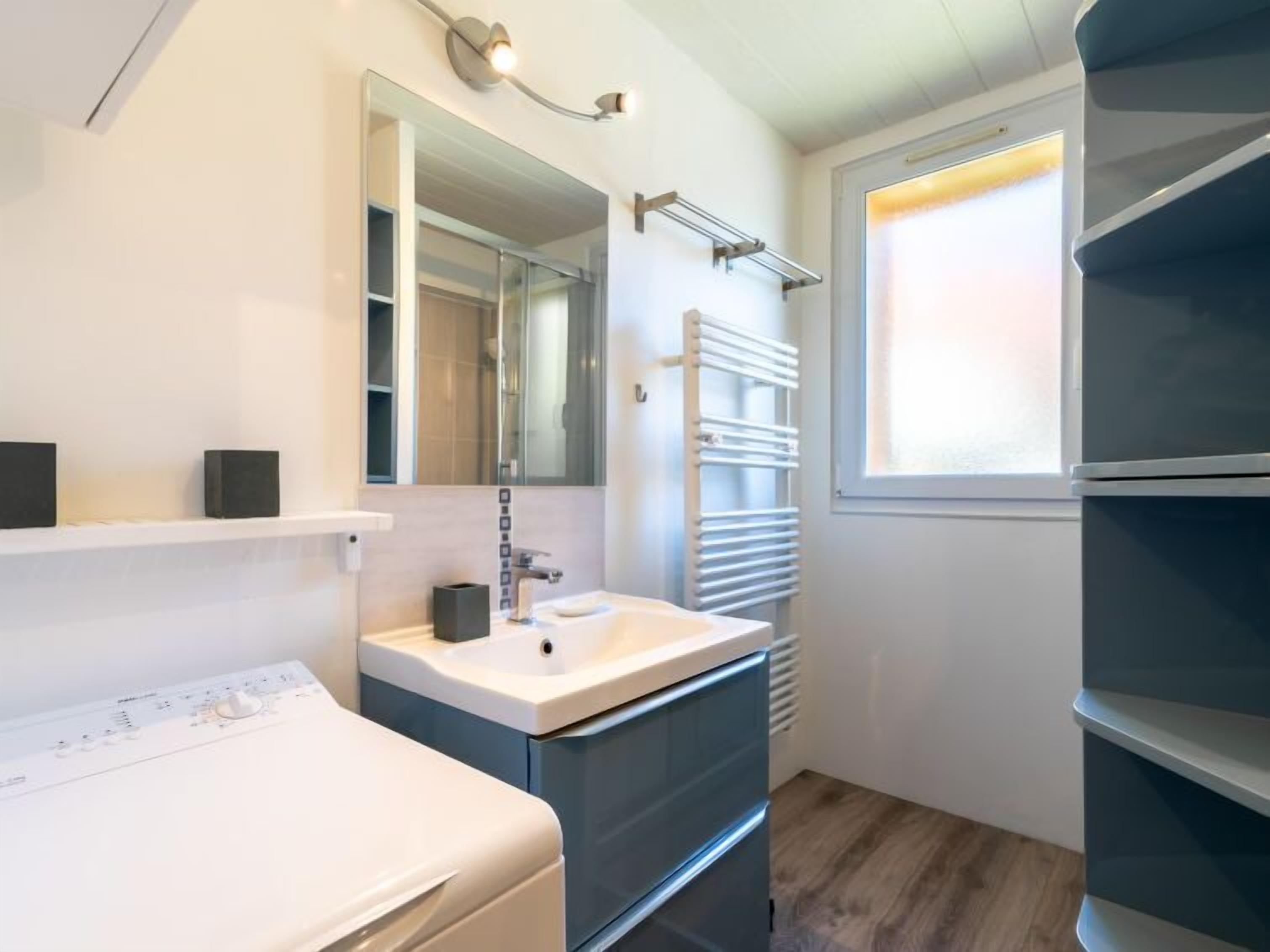A modern bathroom with a white sink, dark cabinetry, a towel rack, and a window with natural light.