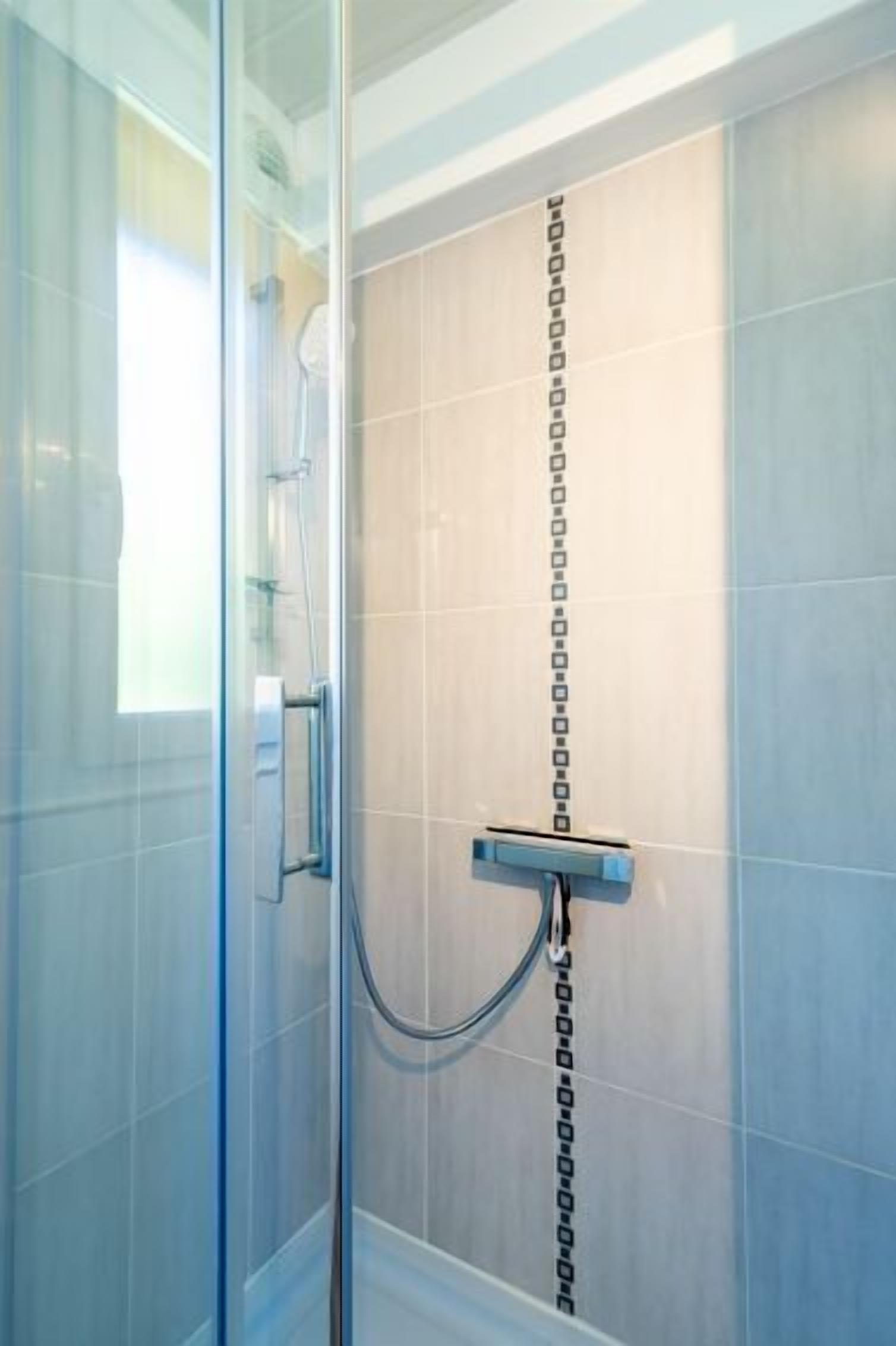 Ducha moderna con cerramiento de vidrio, una franja vertical negra en la pared y cabezal de ducha cromado.