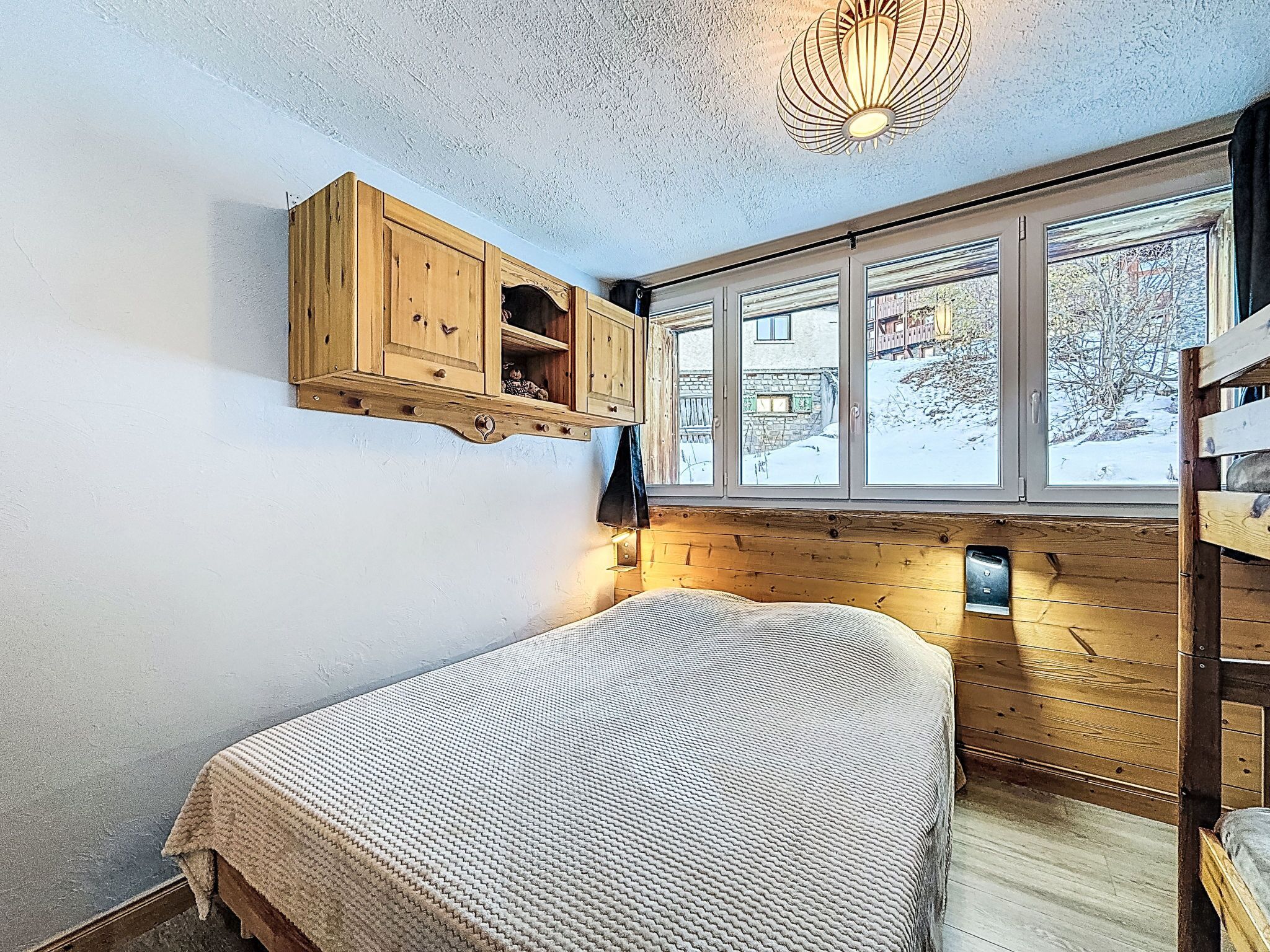 Un dormitorio acogedor con literas, paredes de madera, una ventana con vistas a un paisaje nevado y una lámpara en el techo.