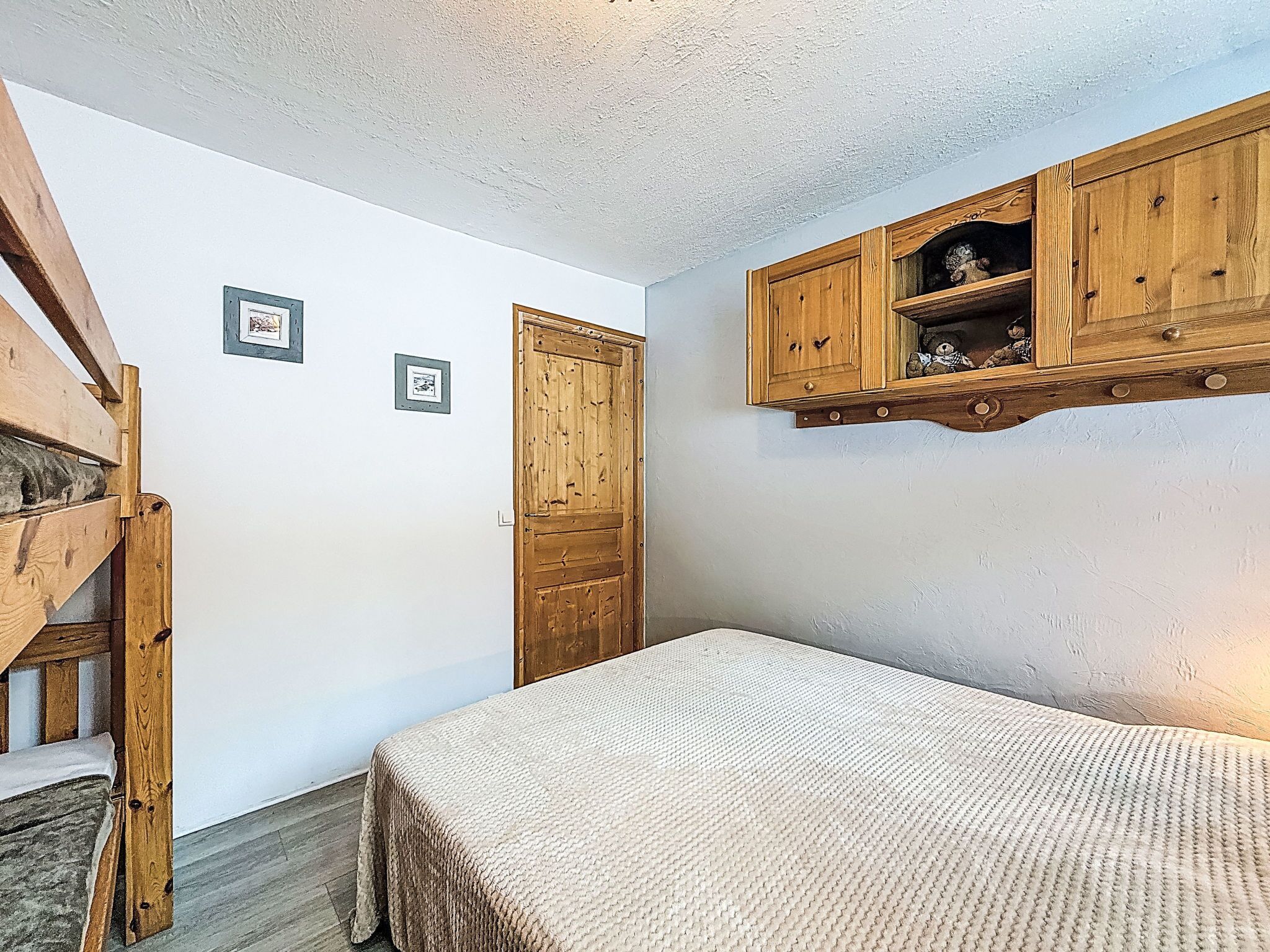 A bedroom with a bed, wooden wardrobe, and two framed pictures on the wall.