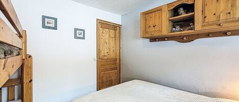 A bedroom with a bed, wooden wardrobe, and two framed pictures on the wall.