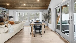 A spacious living area with a wooden ceiling, a beige sofa, a dining table with chairs, and large windows offering a view of the outdoors. - ✨ Secluded Luxury w/ Hot Tub, Firepit, Bar + Ultimate Privacy & Views (Ellicottville)