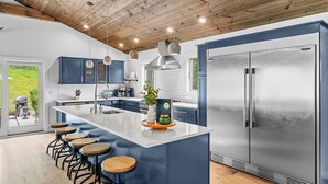 A modern kitchen with a large island, bar stools, and a stainless steel refrigerator. - ✨ Secluded Luxury w/ Hot Tub, Firepit, Bar + Ultimate Privacy & Views (Ellicottville)