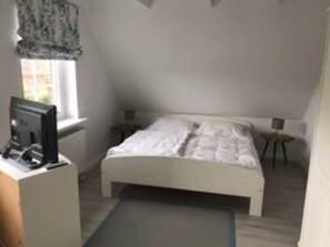 A bedroom with a bed, a desk with a computer, a window with curtains, and a small stool. - Residenz am Meer - Näher am Strand Können Sie Ihren Urlaub Nicht Verbringen! (Utersum)
