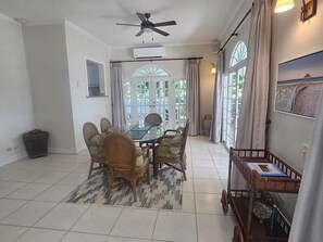 A dining area with a glass table, wooden chairs, a ceiling fan, and large windows with curtains. - 'Bago Breeze' a blissful 4-bdrm villa by the Sea (Lowlands)