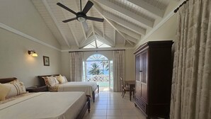 Habitación de hotel con dos camas, un ventilador de techo, un mueble de madera grande y vistas al océano a través de una ventana.