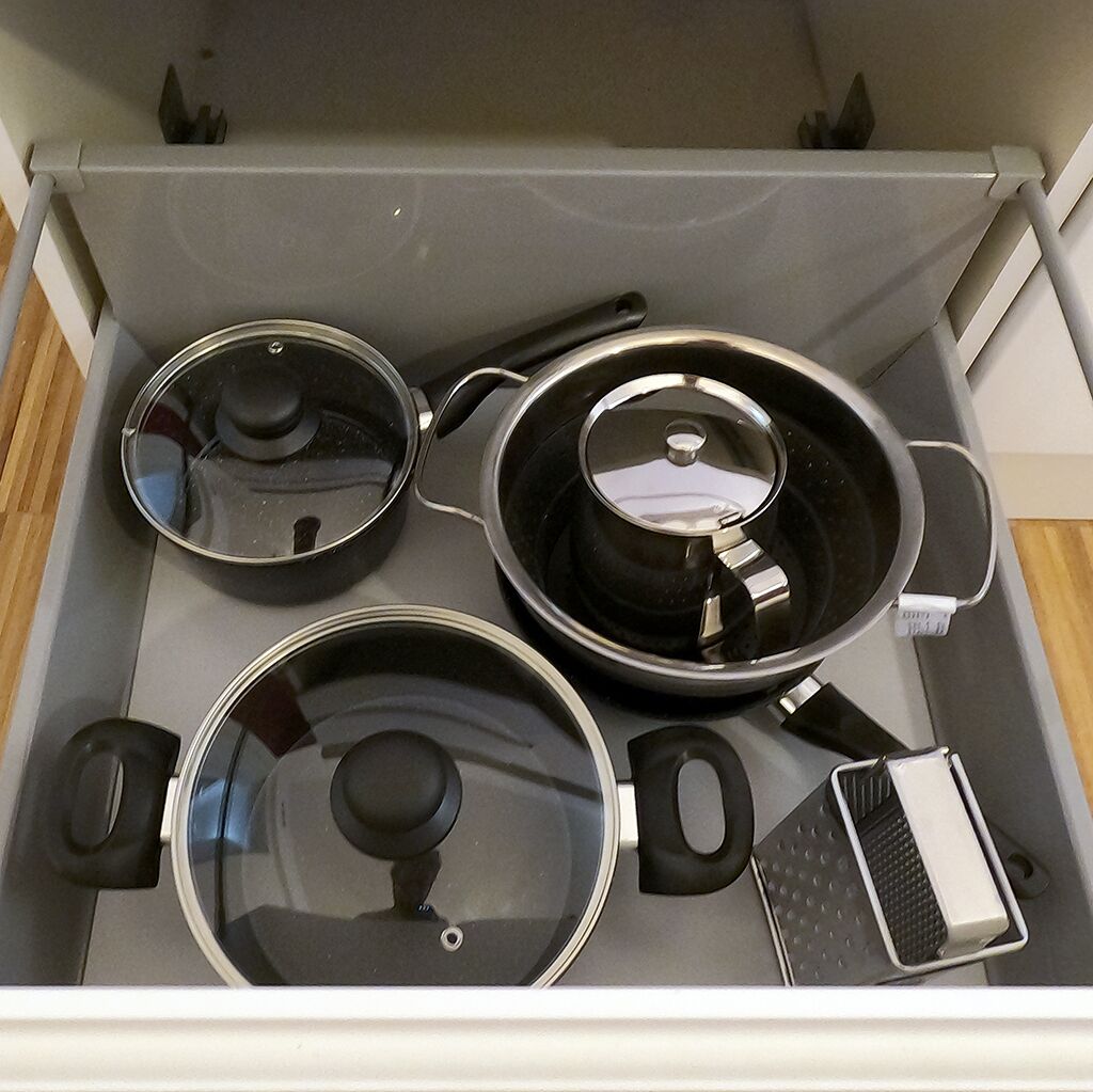 Eine Küchenschublade mit drei Töpfen und einer Reibe.