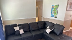 Ein schwarzes Ecksofa mit weiß-schwarzen Kissen in einem Raum mit Holzboden und einer Karte an der Wand.