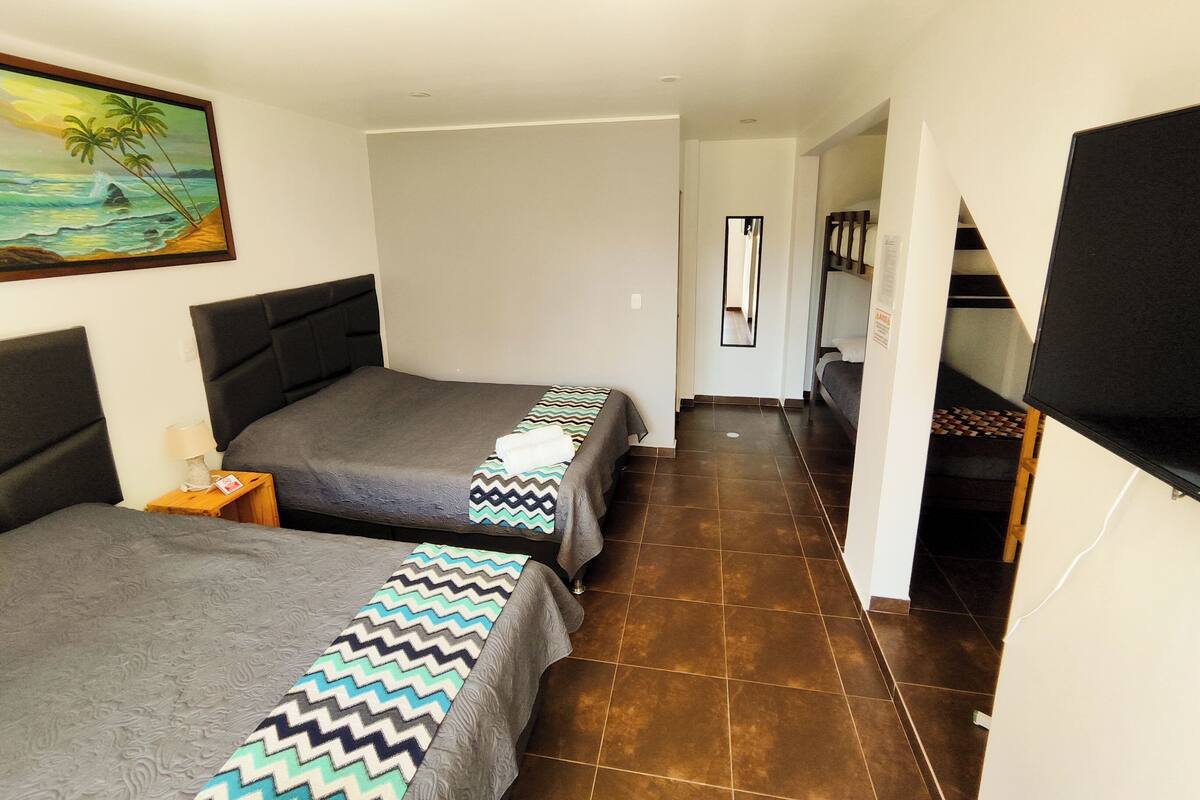 Een hotelkamer met twee bedden, een schilderij van een strandgezicht, een spiegel en een televisie aan de muur.