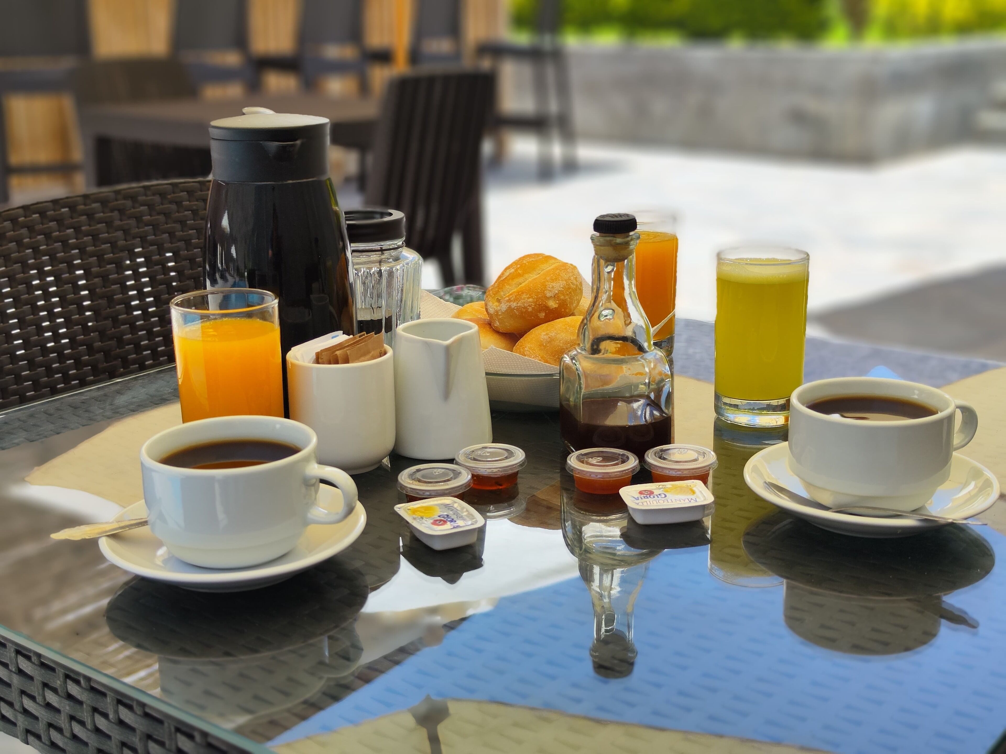 A breakfast setup with coffee, juice, and pastries on a glass table outdoors.
