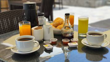 A breakfast setup with coffee, juice, and pastries on a glass table outdoors.
