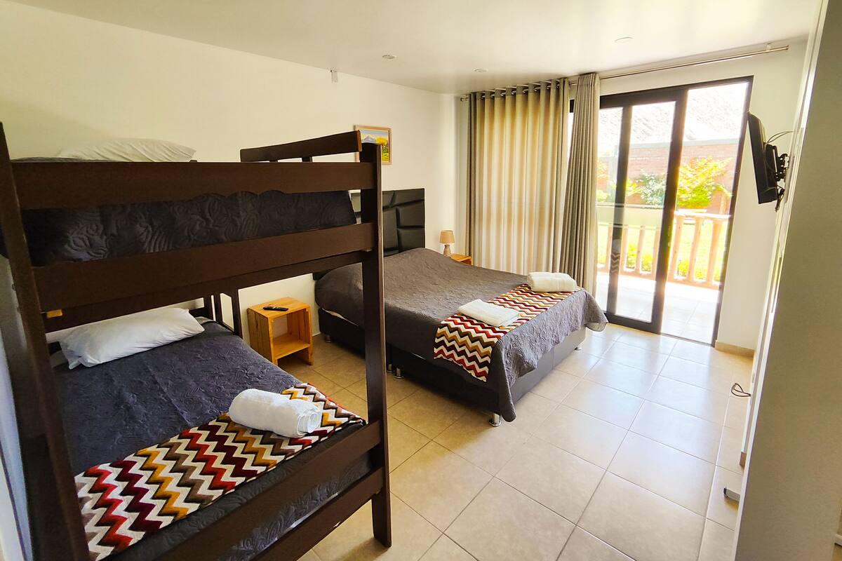 Een hotelkamer met twee stapelbedden, een klein houten nachtkastje, een lamp en een schuifdeur naar een balkon.