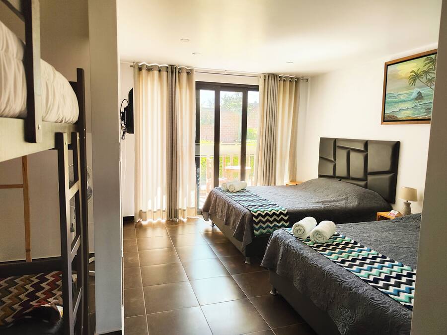 Habitación de hotel con dos camas, un ventanal con cortinas, un ventilador y un cuadro en la pared.
