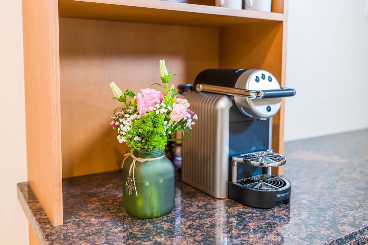 Eine Küchenarbeitsplatte mit einer Kaffeemaschine, einem Blumenkrug und einem Regal mit Tassen und Gläsern.