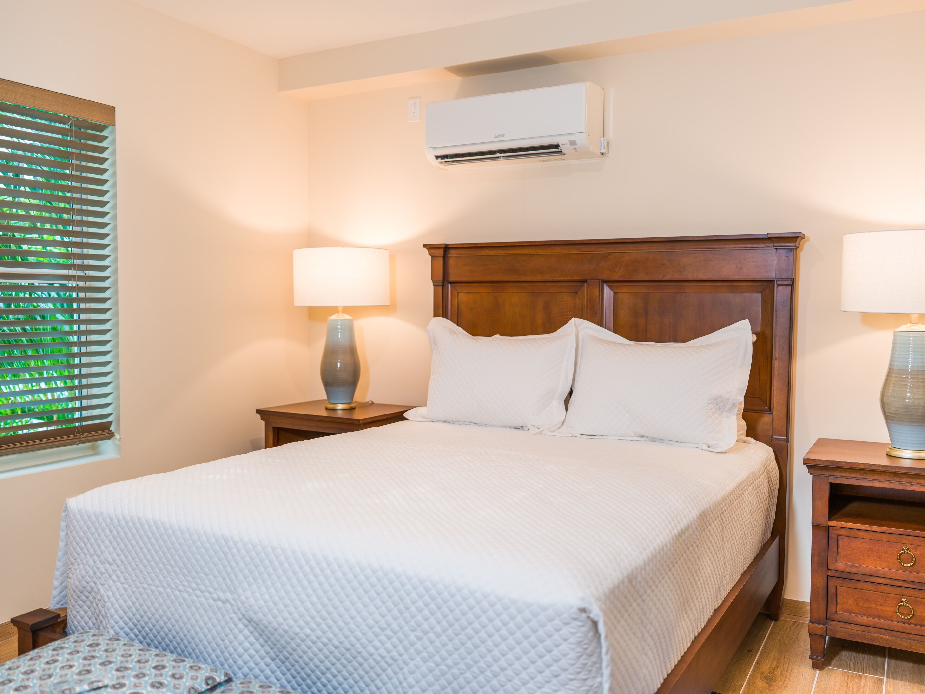 A neatly made bed with white bedding, a wooden headboard, and two bedside tables with lamps.