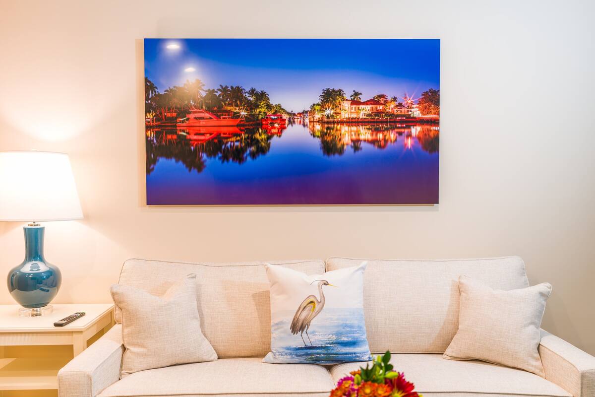 Ein Wohnzimmer mit einer Couch, einem Gemälde einer Nachtszene, einer Lampe und einer Vase mit Blumen.