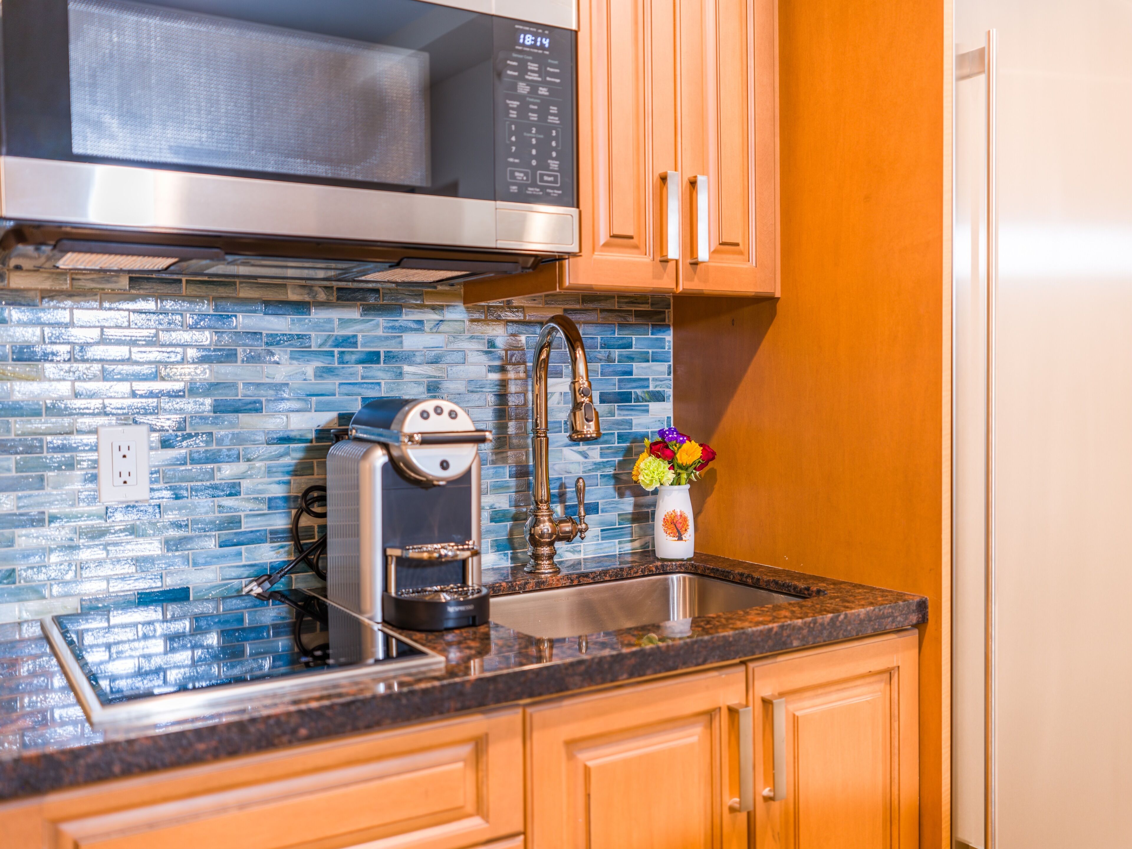 A kitchen with a stainless steel microwave, a coffee maker, a sink, and wooden cabinets.