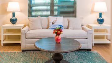 Un soggiorno con un divano beige, due tavolini laterali con lampade, un tavolino rotondo con un vaso di fiori e un tappeto decorato.