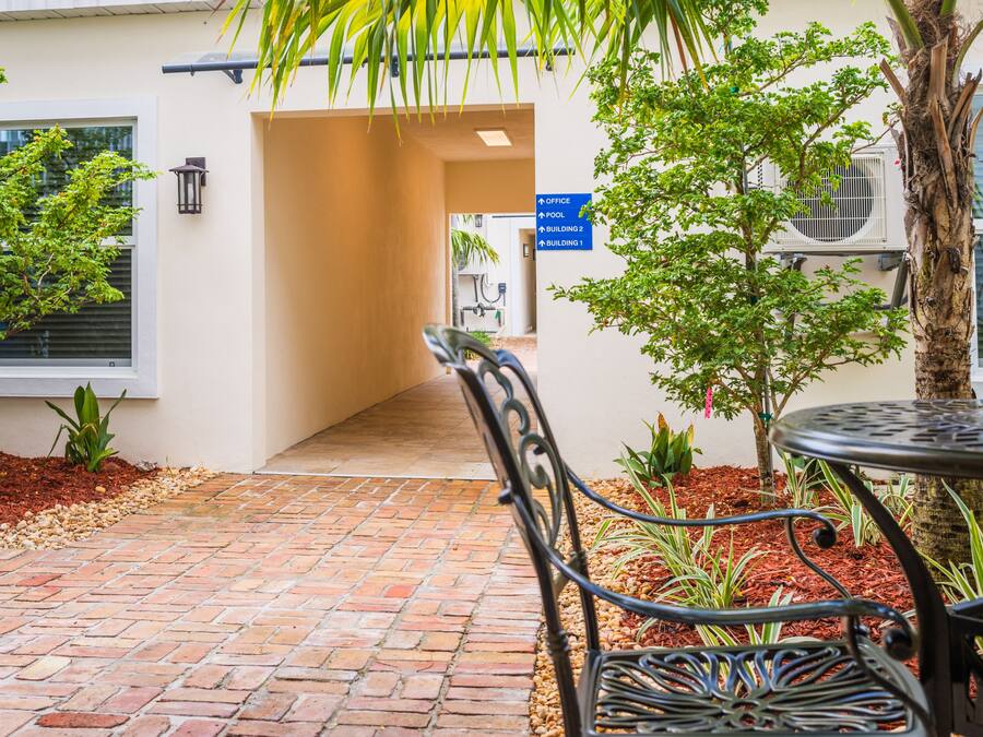 Un chemin pavé de briques menant à l’entrée d’un bâtiment, une chaise en métal et une petite table.