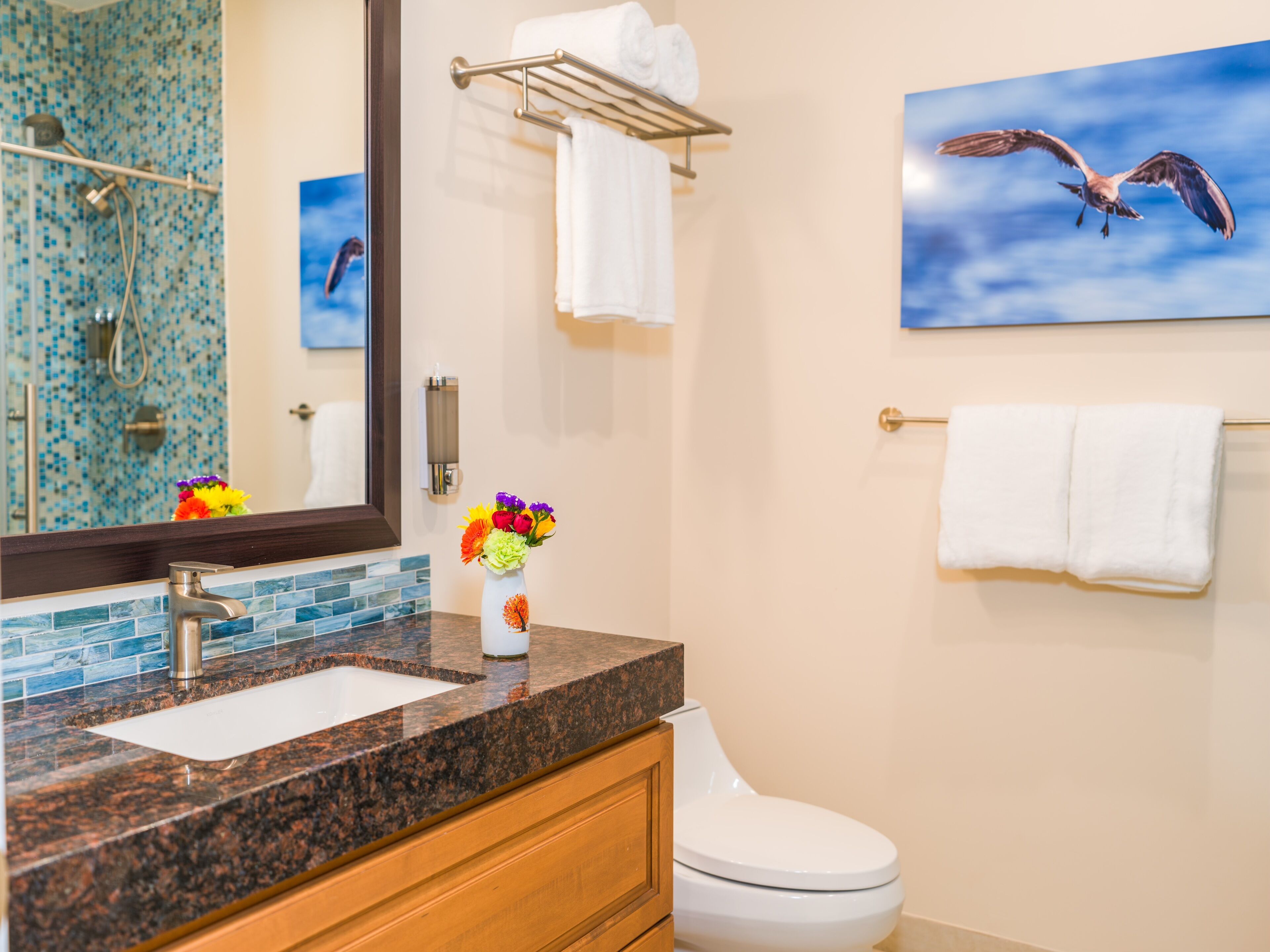 A bathroom with a granite countertop, a white sink, a toilet, a towel rack, and a mirror.
