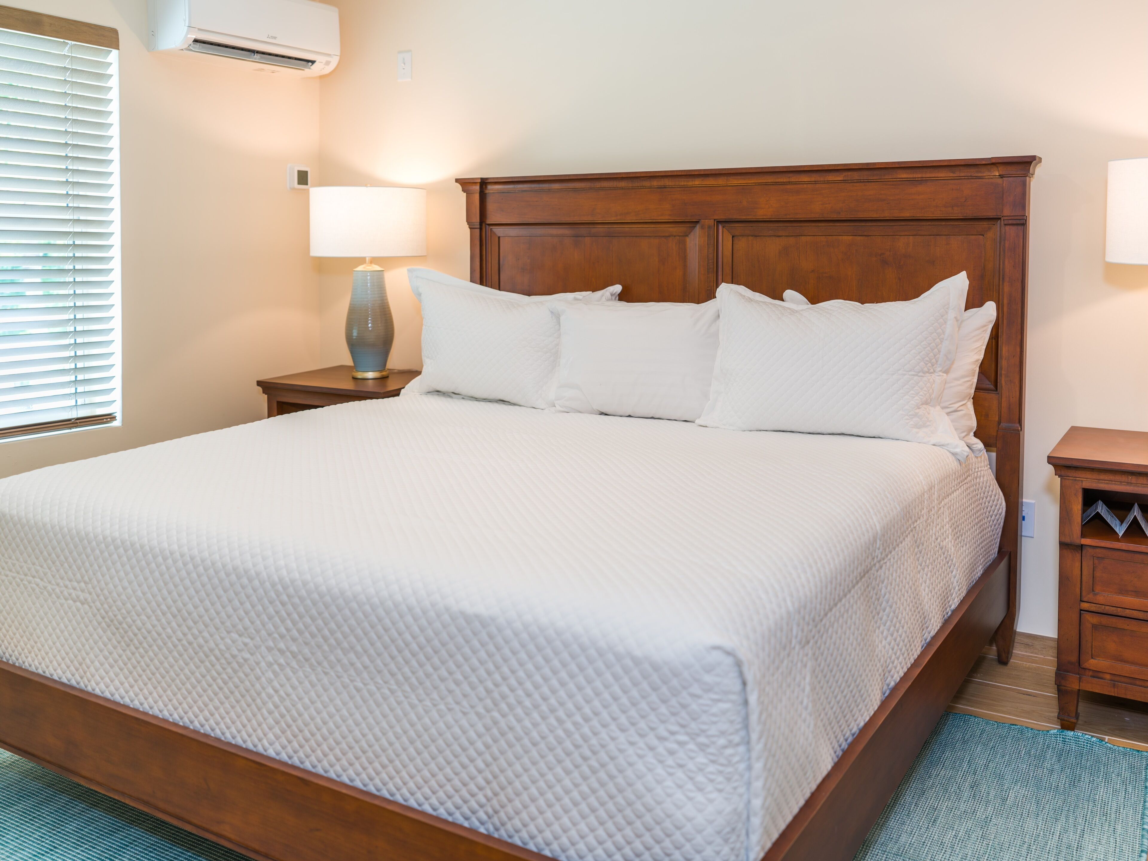 A neatly made bed with a wooden headboard, a bedside lamp, and a small wooden nightstand.