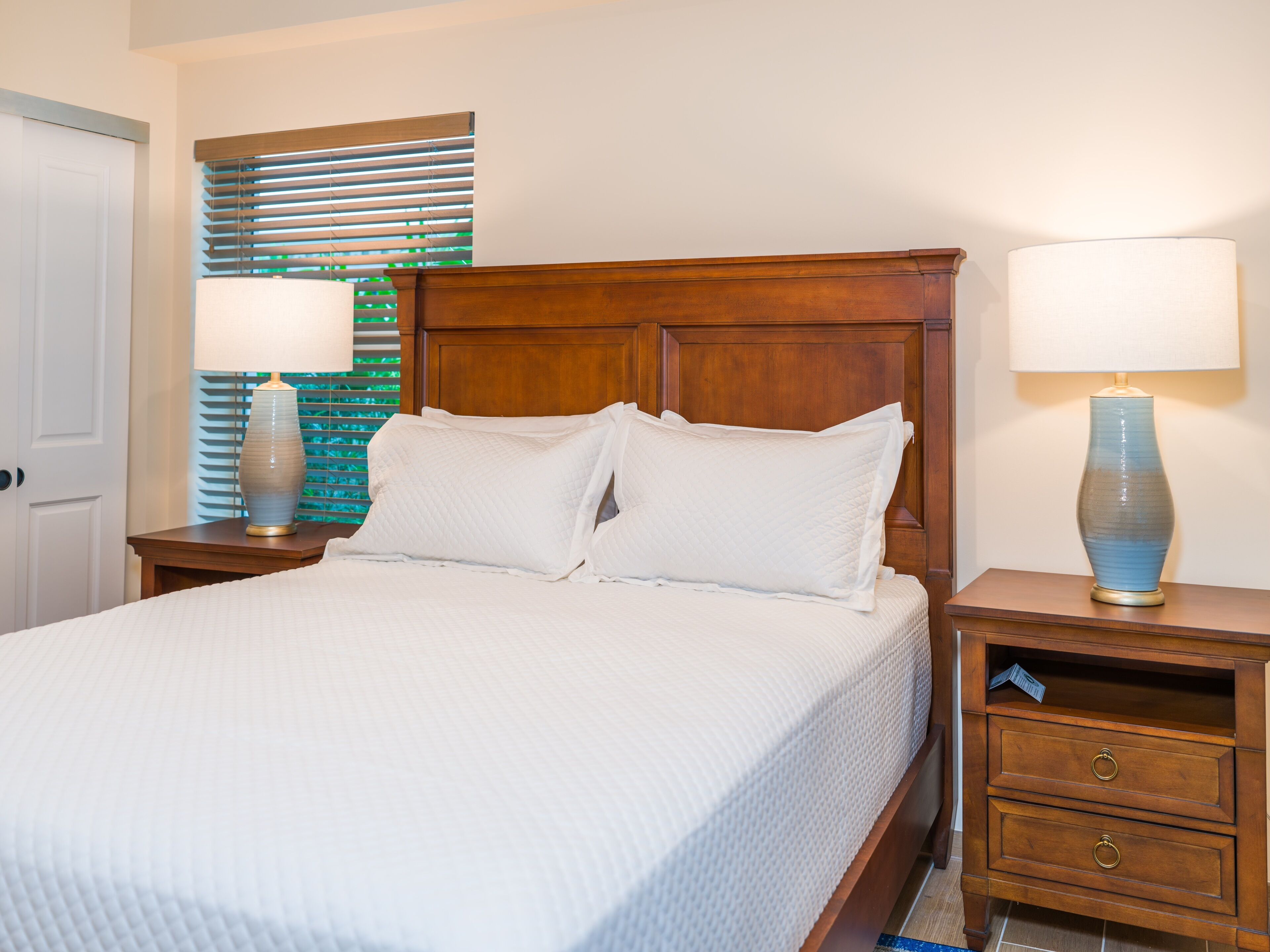 A neatly made bed with white bedding, two bedside tables with lamps, and a wooden headboard.