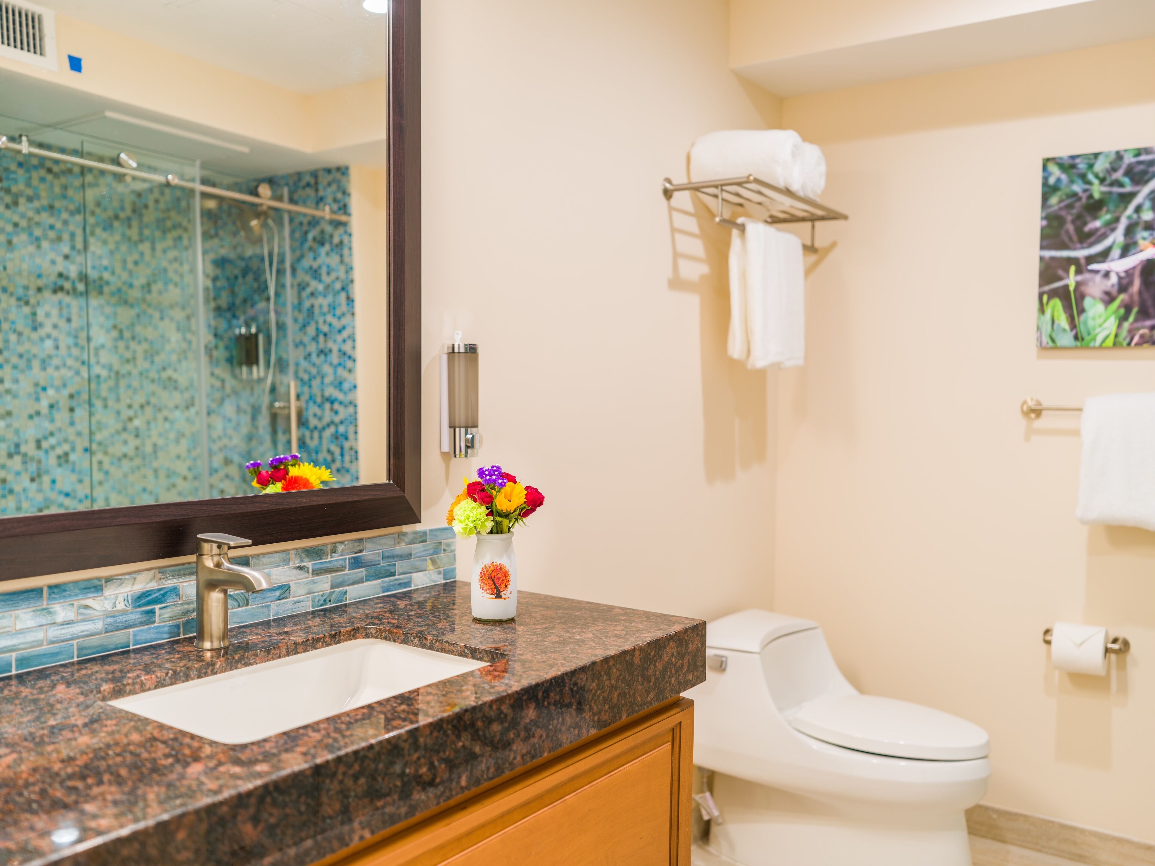 A bathroom with a granite countertop, a sink, a mirror, a toilet, and a towel rack.