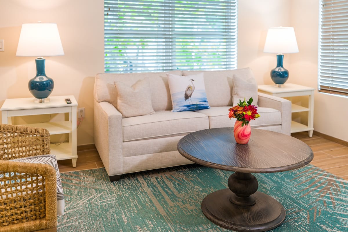 Ein Wohnzimmer mit einem beigen Sofa, zwei Beistelltischen mit Lampen, einem runden Couchtisch mit einer Vase und einem gemusterten Teppich.