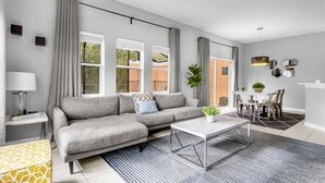 A modern living room with a grey sofa, a coffee table, and a dining area with a table and chairs. - Terra verde resort 4brs / 3bth cozy Townhome (Kissimmee)