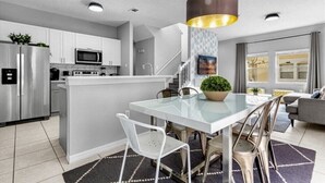 A modern kitchen with white cabinets, a stainless steel refrigerator, a microwave, and a glass dining table with chairs. - Terra verde resort 4brs / 3bth cozy Townhome (Kissimmee)