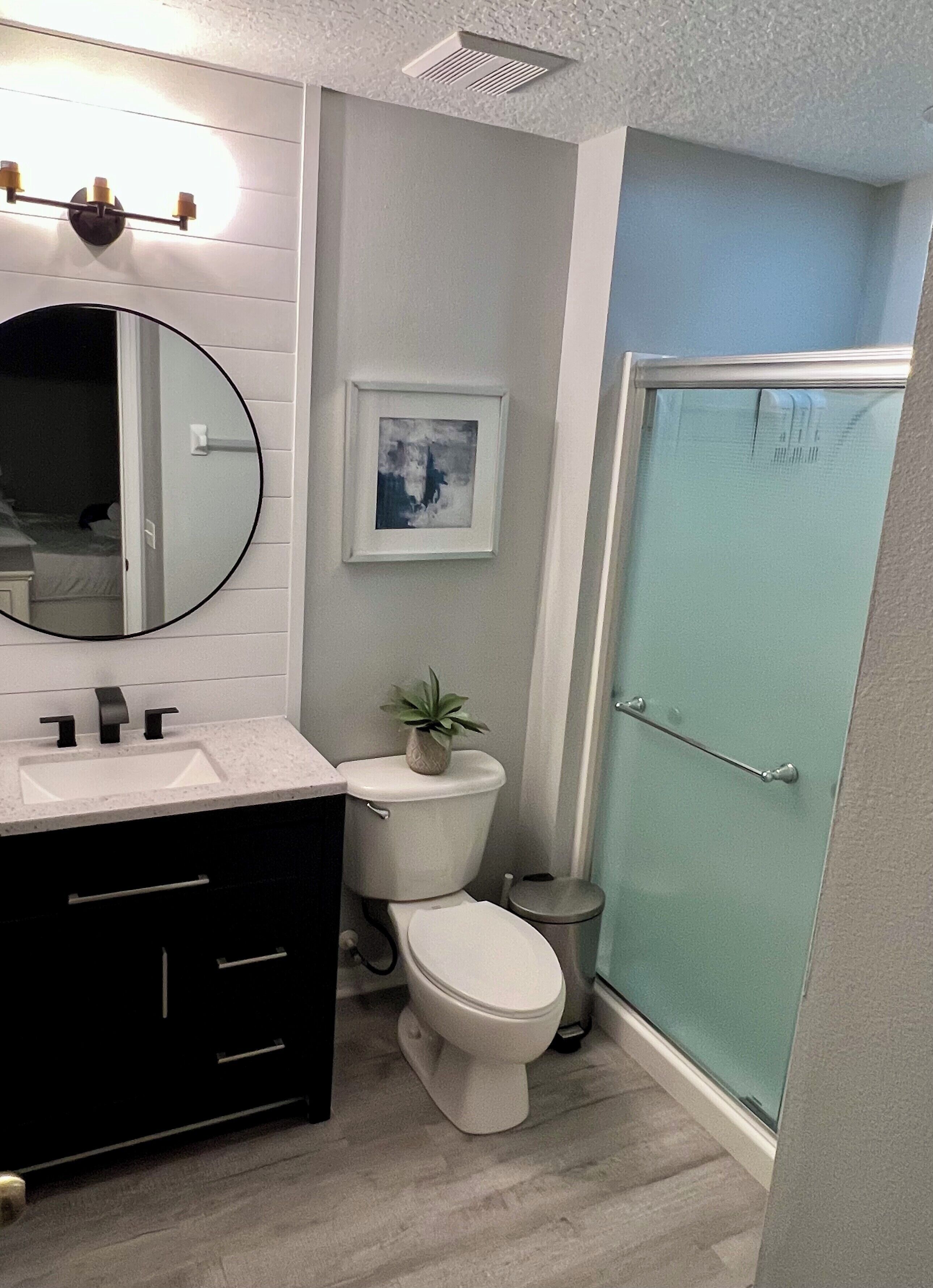 A modern bathroom with a white sink, black vanity, a toilet, and a glass shower enclosure.