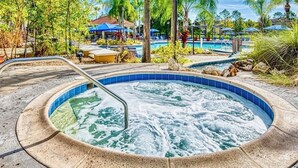 A hot tub surrounded by palm trees and a pool area with umbrellas. - Terra verde resort 4brs / 3bth cozy Townhome (Kissimmee)