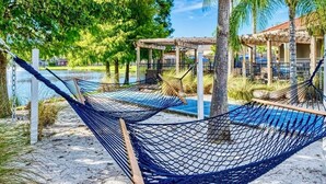 A hammock by a poolside with a wooden pergola and palm trees in the background. - Terra verde resort 4brs / 3bth cozy Townhome (Kissimmee)