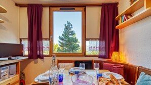 A cozy dining area with a table set for two, a television, and a window with a view of trees. - Vostok Zodiaque by Interhome (Le Corbier)