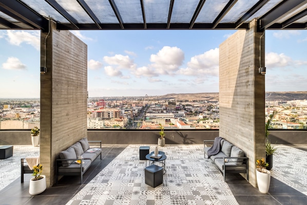 A rooftop terrace with a city view, featuring a sofa, chairs, a coffee table, and potted plants.